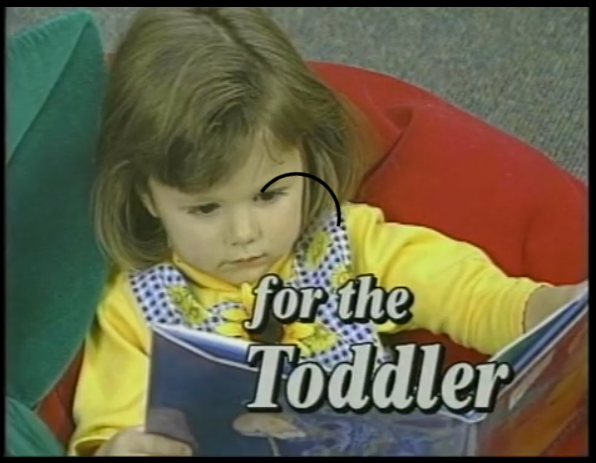 A little girl is reading a book in her chair.